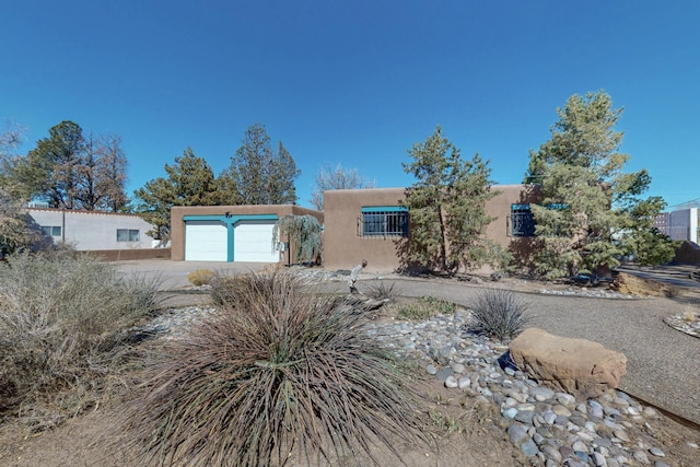 pueblo-style house featuring driveway, an attached garage, and stucco siding