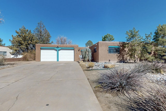 pueblo-style home featuring concrete driveway, an attached garage, and stucco siding