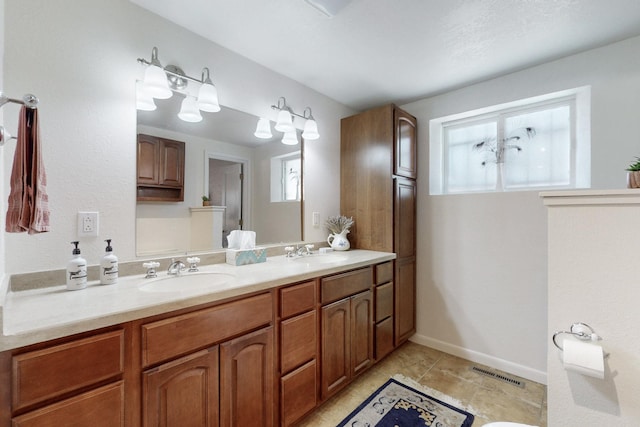 bathroom with double vanity, a sink, visible vents, and baseboards