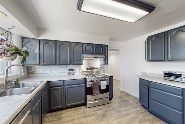 kitchen featuring under cabinet range hood, a sink, light countertops, appliances with stainless steel finishes, and tasteful backsplash