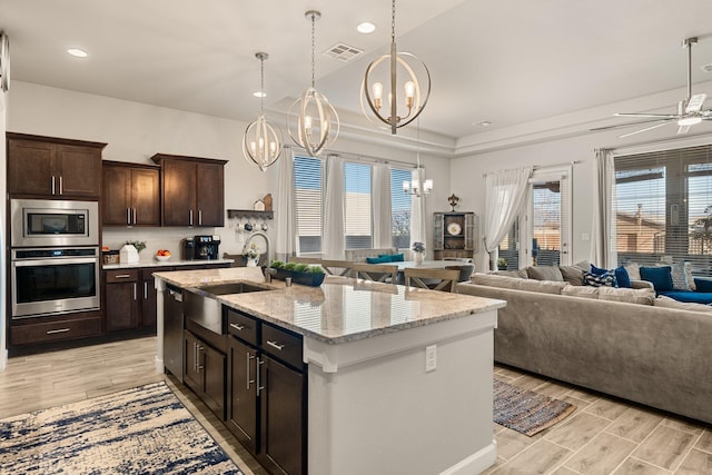 kitchen featuring wood finish floors, a sink, visible vents, open floor plan, and appliances with stainless steel finishes