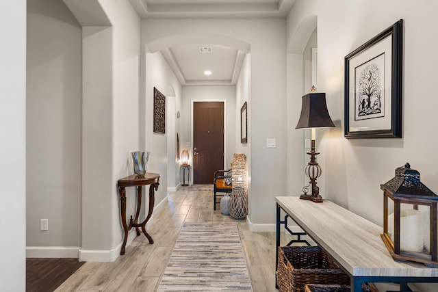 hallway featuring arched walkways, light wood-type flooring, visible vents, and baseboards