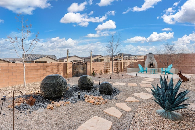 view of yard with a patio, exterior fireplace, fence, and a gate