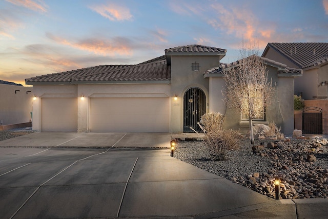 mediterranean / spanish home featuring a garage, a tile roof, driveway, a gate, and stucco siding