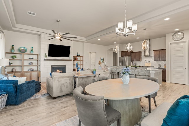 dining room with light wood-style flooring, a fireplace, visible vents, and a raised ceiling