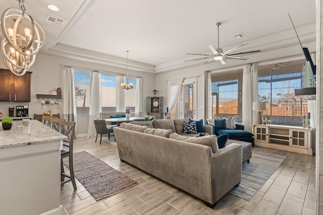 living room featuring ceiling fan with notable chandelier, visible vents, a tray ceiling, and wood finish floors