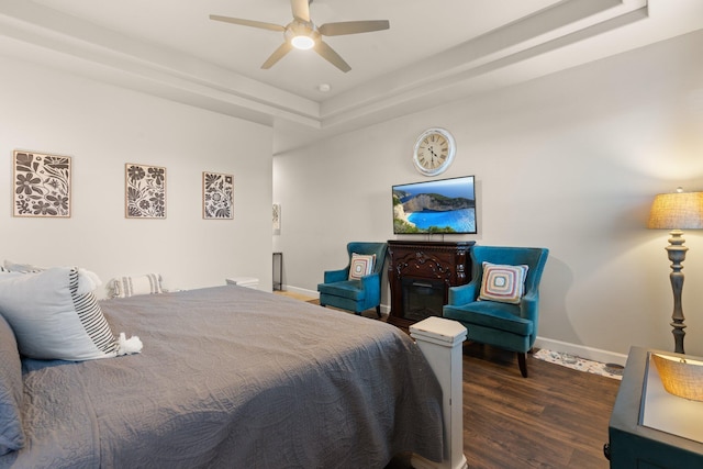 bedroom featuring a raised ceiling, wood finished floors, a ceiling fan, and baseboards