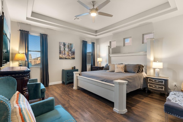 bedroom with dark wood-style floors, baseboards, a raised ceiling, and a ceiling fan