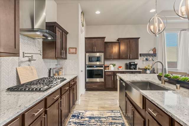 kitchen featuring dark brown cabinetry, a sink, appliances with stainless steel finishes, light stone countertops, and wall chimney exhaust hood