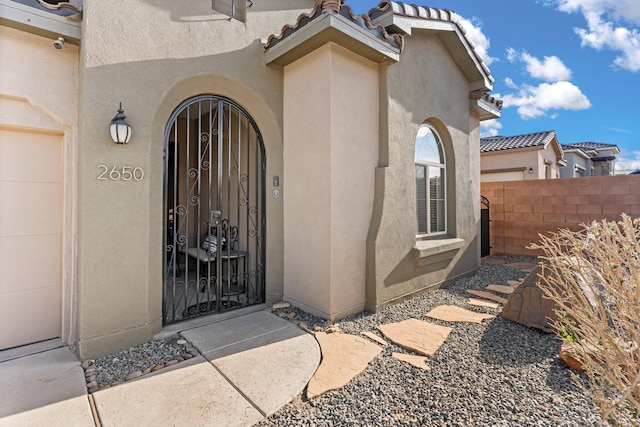 view of exterior entry featuring a tile roof, fence, and stucco siding