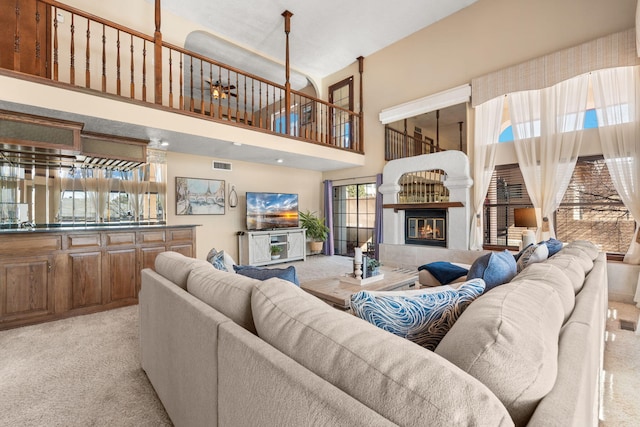 living area featuring a towering ceiling, light colored carpet, visible vents, and a tiled fireplace