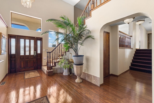 entryway with a towering ceiling, wood-type flooring, visible vents, and arched walkways