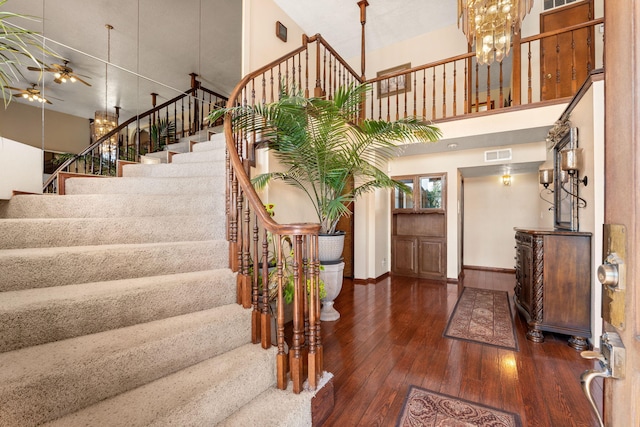 entryway featuring hardwood / wood-style flooring, visible vents, stairway, a towering ceiling, and ceiling fan with notable chandelier