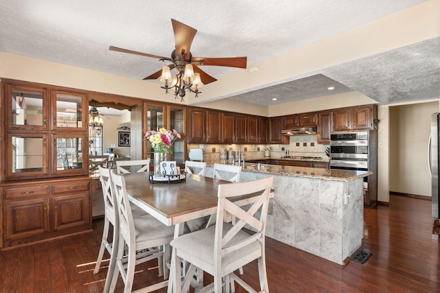 dining room featuring dark wood-style floors, visible vents, a ceiling fan, a textured ceiling, and baseboards