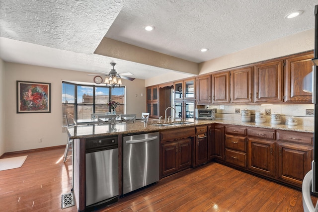 kitchen with light stone counters, dark wood-style flooring, a peninsula, a sink, and stainless steel dishwasher