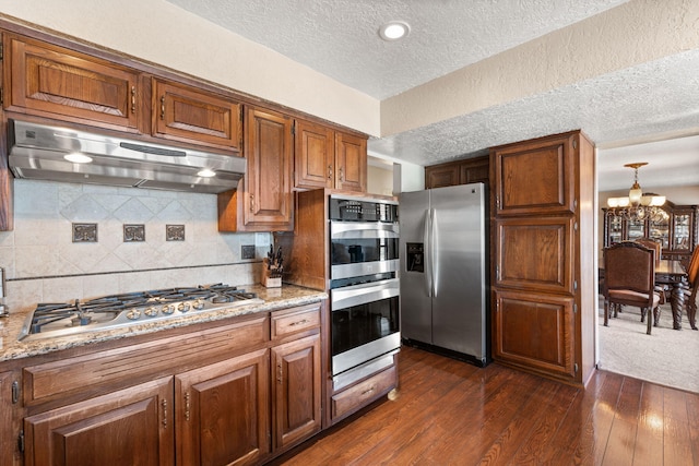 kitchen with decorative backsplash, dark wood-style flooring, stainless steel appliances, a textured ceiling, and under cabinet range hood