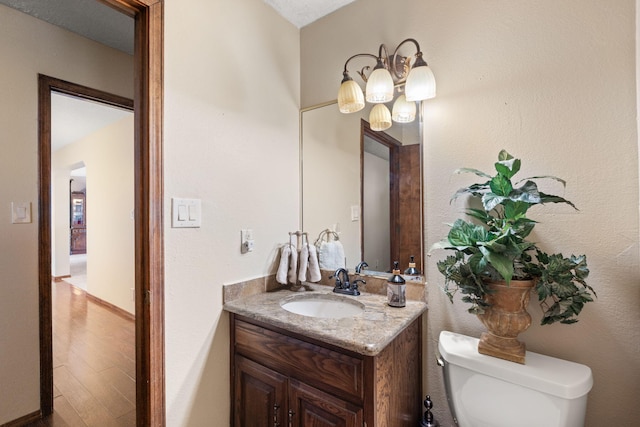 bathroom featuring toilet, baseboards, wood finished floors, and vanity