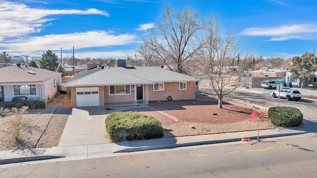 ranch-style home featuring metal roof, driveway, an attached garage, and stucco siding