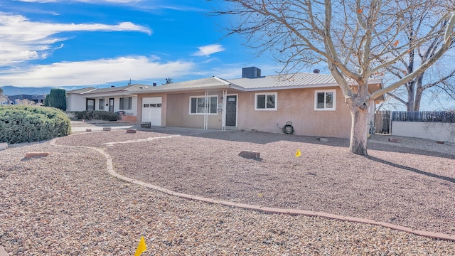 rear view of property with a garage, metal roof, fence, and stucco siding