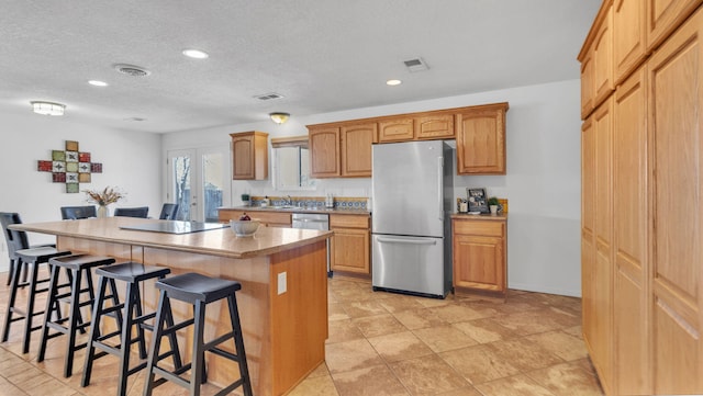 kitchen with a breakfast bar area, visible vents, appliances with stainless steel finishes, a kitchen island, and a textured ceiling