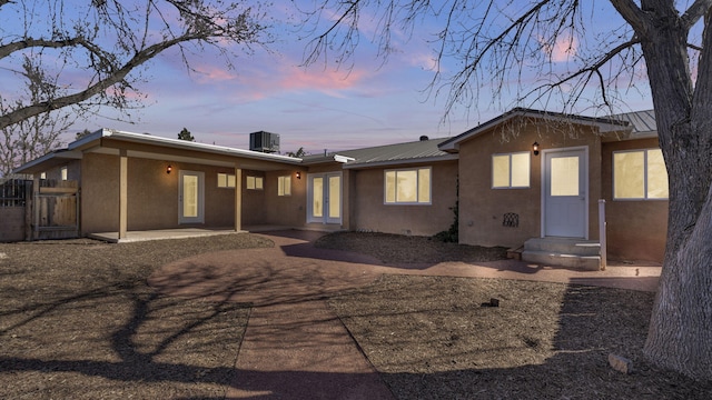 back of house at dusk with metal roof, central AC, french doors, stucco siding, and a patio area