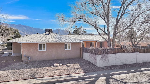 view of side of home with a fenced front yard, a mountain view, metal roof, and stucco siding