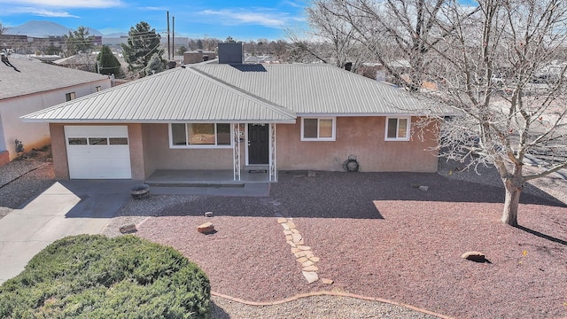 ranch-style home with metal roof, an attached garage, driveway, and stucco siding