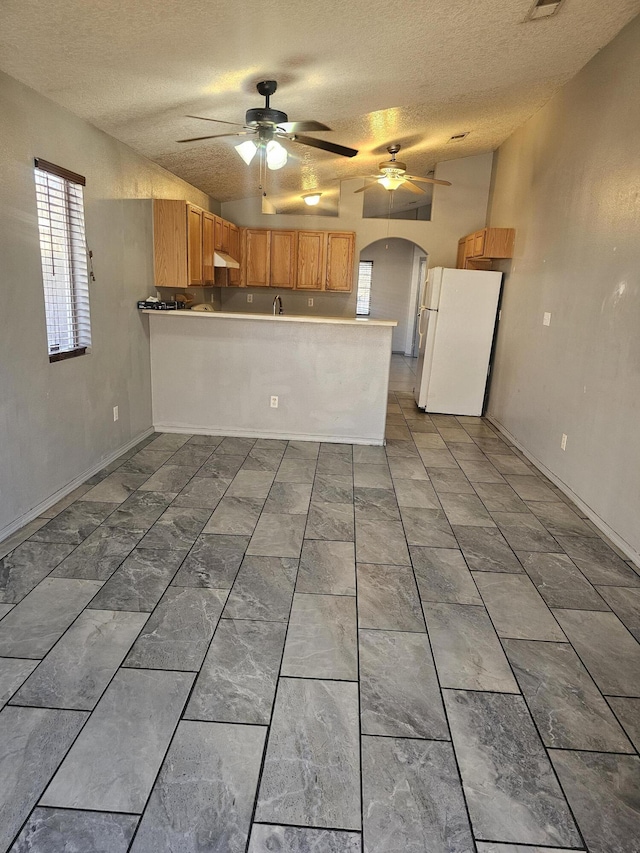 kitchen featuring a peninsula, arched walkways, a ceiling fan, and freestanding refrigerator