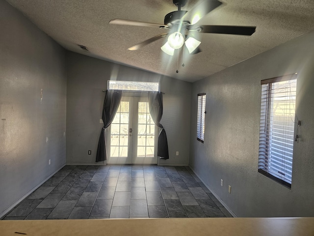 spare room with a healthy amount of sunlight, a textured wall, vaulted ceiling, and french doors