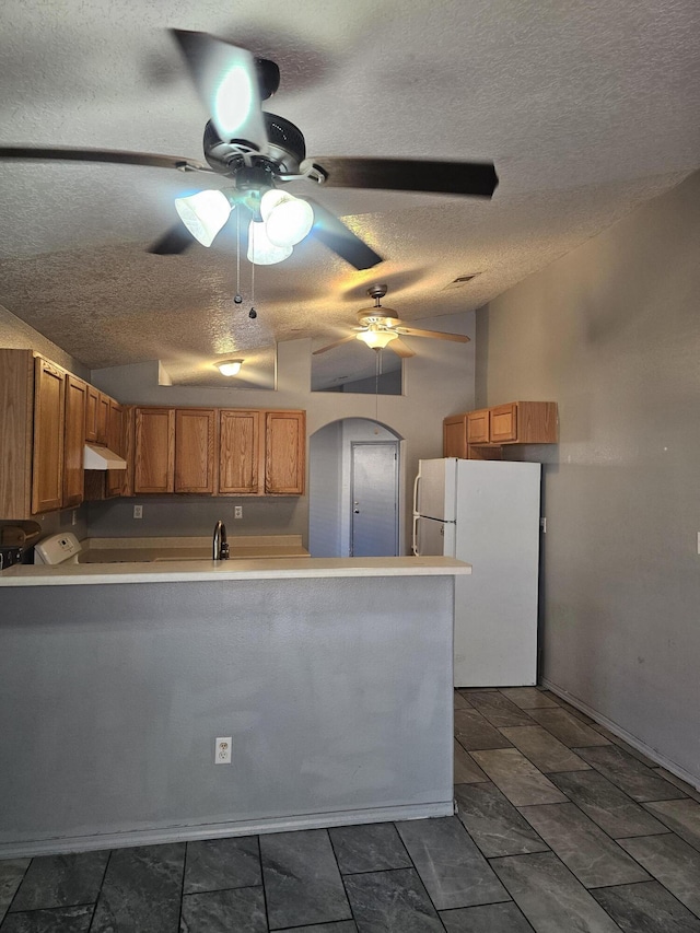 kitchen featuring arched walkways, light countertops, freestanding refrigerator, a peninsula, and under cabinet range hood