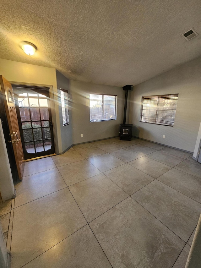 unfurnished living room featuring light tile patterned floors, a textured ceiling, lofted ceiling, visible vents, and a wood stove