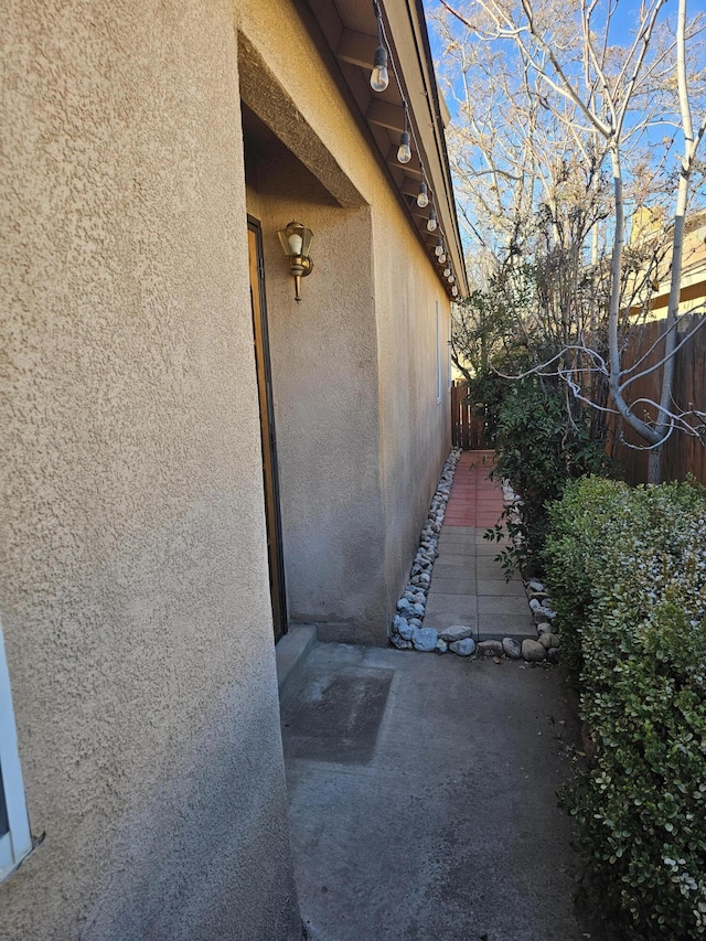 view of side of home with a patio area, fence, and stucco siding