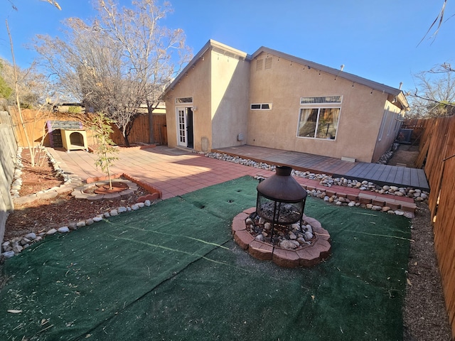 back of property with a fenced backyard, a fire pit, an outbuilding, and stucco siding