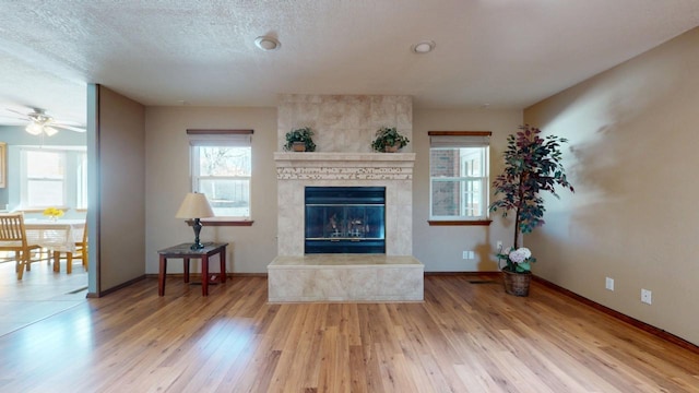 living area with wood-type flooring, a large fireplace, a textured ceiling, and baseboards