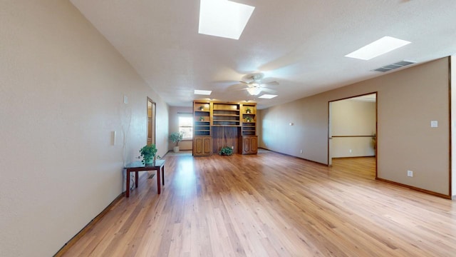 unfurnished living room featuring a ceiling fan, a skylight, visible vents, and light wood finished floors