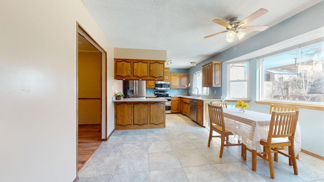 kitchen with a textured ceiling, stainless steel appliances, a sink, light countertops, and brown cabinetry