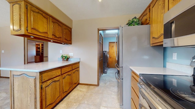 kitchen featuring stainless steel appliances, brown cabinetry, a peninsula, and light countertops