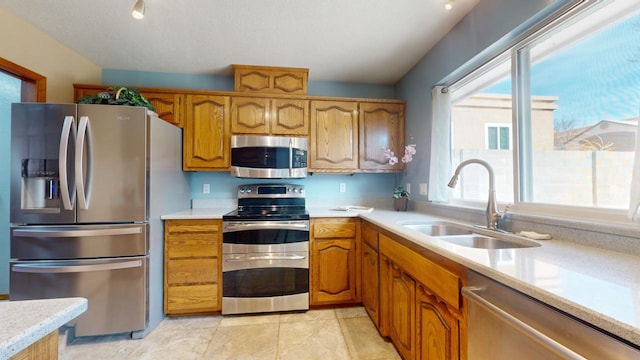 kitchen with stainless steel appliances, brown cabinetry, a sink, and light countertops