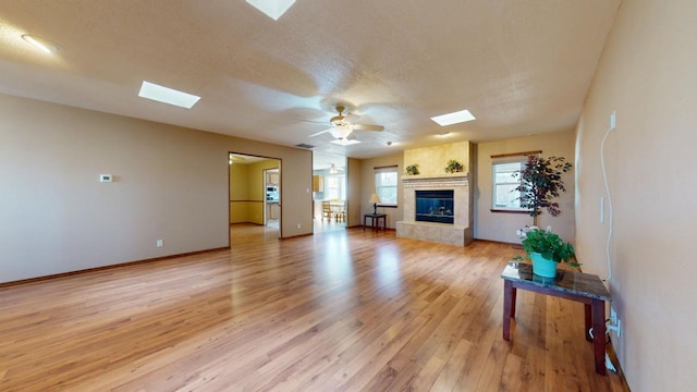 living room featuring light wood-style floors, a skylight, a large fireplace, and a textured ceiling