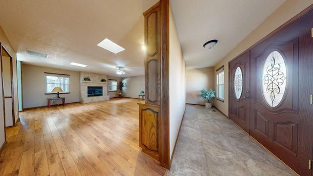 foyer with a skylight, a fireplace, light wood finished floors, visible vents, and a textured ceiling