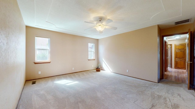 empty room featuring a ceiling fan, visible vents, light carpet, and a textured ceiling