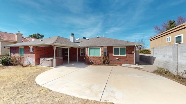 back of house with brick siding, a patio area, and a hot tub