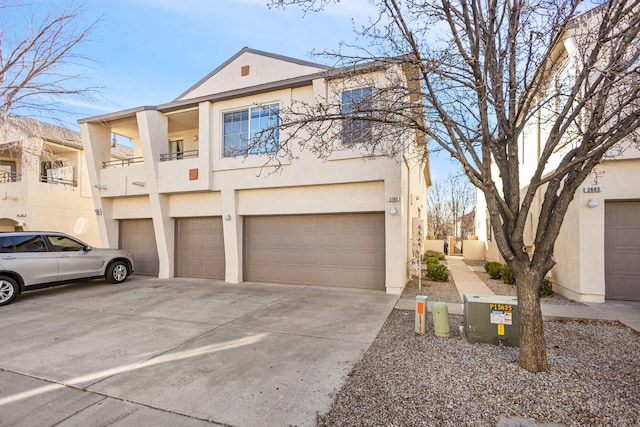 view of front of property featuring driveway, an attached garage, a balcony, and stucco siding