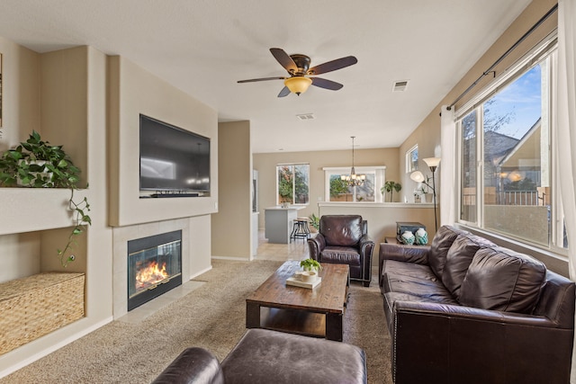 living room with carpet, a fireplace, visible vents, and ceiling fan with notable chandelier