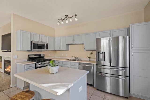 kitchen with light tile patterned floors, a glass covered fireplace, light countertops, stainless steel appliances, and a sink