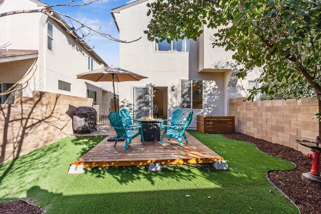 rear view of house with an outdoor fire pit, a lawn, fence private yard, a wooden deck, and stucco siding