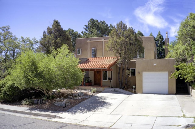 pueblo revival-style home featuring a tile roof, stucco siding, a porch, concrete driveway, and an attached garage