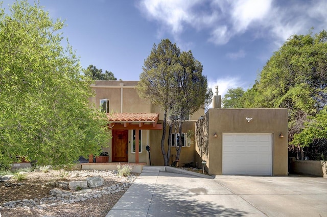 pueblo-style house with a garage, concrete driveway, a tiled roof, and stucco siding