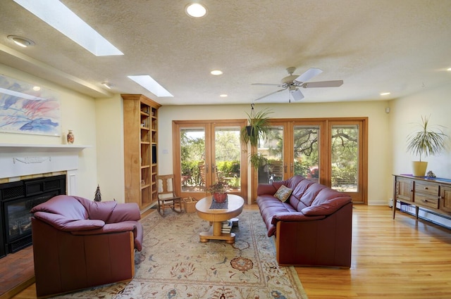 living area with a textured ceiling, recessed lighting, a skylight, wood finished floors, and a glass covered fireplace