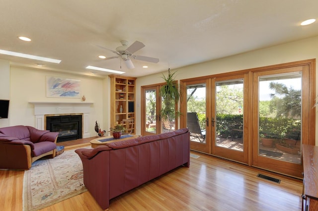 living area with visible vents, a glass covered fireplace, light wood-style flooring, and recessed lighting